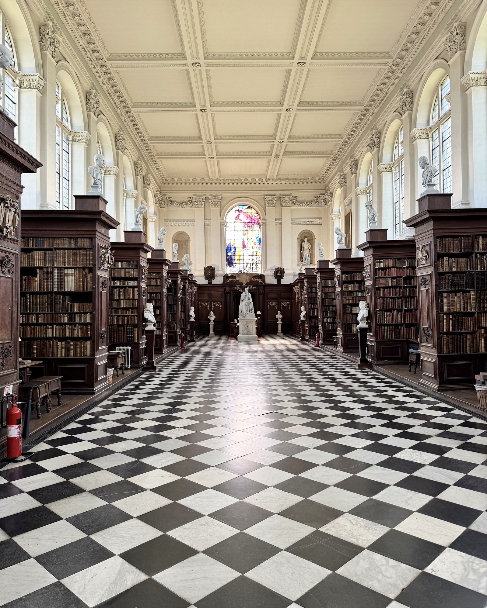 A symmetrical view through a historic Cambridge library hall with a chequered floor, dark bookcases and an ornate ceiling